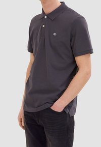 Polo gris foncé en coton, avec un col classique, trois boutons, des manches courtes et un petit logo sur la poitrine.