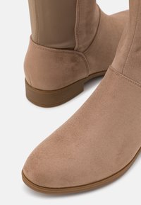 Beige nubuk bokacipő, sima felülettel, kerek orral és alacsony barna gumitalppal. Az oldalsó panelek azonos anyagból készültek.