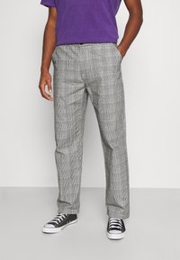 Gray plaid trousers made of textured fabric, featuring a relaxed fit, side pockets, and paired with black sneakers for a casual look.