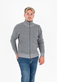 Grijze ritssweater met een hoge kraag, gemaakt van een geweven stof met textuur, afgewerkt met geribbelde mouwen en zoom, gedragen met een blauwe jeans.