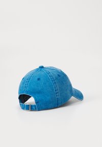 Casquette de baseball en denim bleu avec une visière incurvée, une sangle ajustable à l'arrière et des détails de couture visibles.