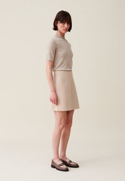 Top de punto beige con mangas cortas, combinado con una falda A-line beige claro y unos mocasines bicolor en marrón. Texturas suaves, diseño minimalista.