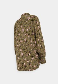 Blusa de tecido verde oliva com padrão floral, apresentando desenhos em rosa e preto, mangas longas com punhos abotoados e gola.