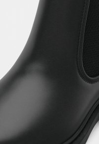 Černé matné Chelsea boty s elastickým bočním panelem a hladkým zaobleným špičkou na bílém pozadí.