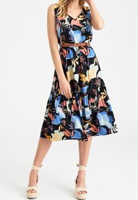 Robe sans manches à motif floral en noir, avec un décolleté en V, une jupe évasée et une taille cintrée avec une ceinture. Accents en rose, bleu et jaune.