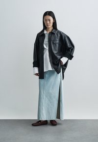 Sort læder oversize skjorte, lys denim maxinederdel med sideslids, hvid skjorte med knapper under, og brune slip-on sko.