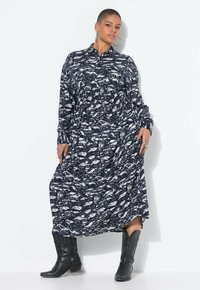 Vestido midi de manga larga con un patrón en blanco y negro, con cuello abotonado, combinado con botas de vaquero negras altas. Presenta detalles fruncidos.
