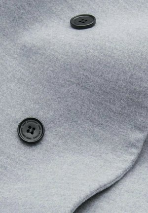 Grau Wollstoff mit glatter Textur und zwei schwarzen Kunststoffknöpfen, die auf einem gefalteten, drapierten Abschnitt des Materials platziert sind.