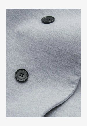 Grijze wollen stof met een gladde textuur en twee zwarte kunststof knopen, gepositioneerd op een gevouwen, gedrapeerd gedeelte van het materiaal.