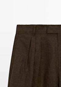 Pantalon en lin marron avec plis devant et passants pour ceinture, présenté de la taille jusqu'au milieu des cuisses sur fond blanc.