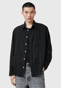 Sorte langærmede skjorte med diskrete lodrette striber, hvide knapper, en forlomma og en afslappet pasform, parret med lysegrå denim.