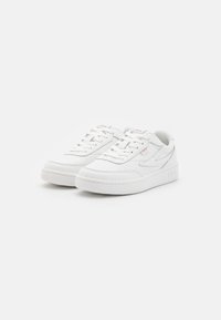Sneaker bianchi con tomaia in pelle liscia, dettagli perforati, colletto imbottito e suola in gomma texturizzata. Presenta sottili accenti con il logo.