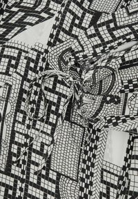 Sort-hvidt mønstret stof med geometriske former, firkanter og linjer. Bundet i taljen med et smalt matchende bånd.