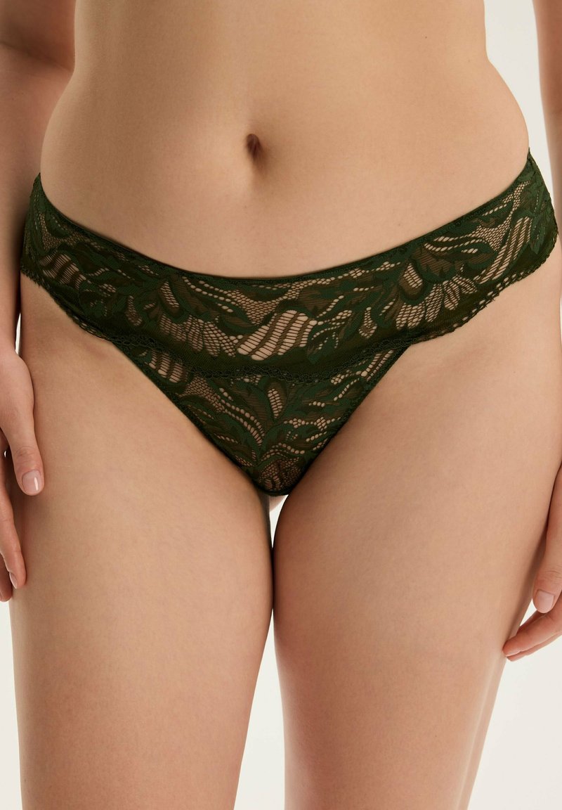 Zielony koronkowy thong z kwiatowymi wzorami, szerokim koronkowym paskiem w talii i półprzezroczystą teksturą, podkreślający szczegółowe detale i design.