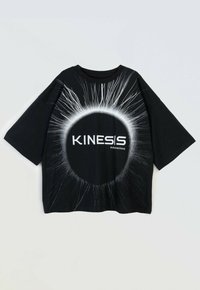 Czarna, oversize koszulka z białym okrągłym wzorem w postaci eksplozji oraz napisem "KINESIS subconscious" na jednolitym tle.