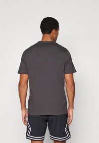 Grå kortærmet t-shirt med rund hals, der har en glat tekstur. Bæres sammen med sorte træningsshorts, hvilket viser et simpelt, afslappet design.
