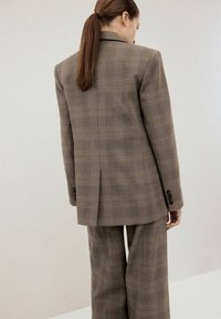 Grijs geruit pak met een op maat gemaakte blazer en wijde broekspijpen. De stof heeft een subtiele textuur en de blazer heeft knoopmanchetten.