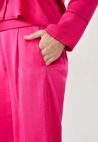 Roze satijnen outfit bestaande uit een top en een broek. De stof heeft een gladde textuur, met een ontspannen pasvorm en zichtbare zijzakken.
