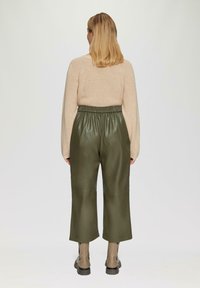 Khaki groene leren broek met een elastieken tailleband, met een wijd ontwerp, gecombineerd met een lichtbeige trui en enkellaarsjes.