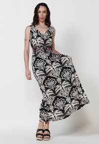 Robe maxi noire et crème à motif floral, présentant un décolleté en V, un corsage ajusté et une jupe fluide, avec des détails ornés au niveau de la taille.