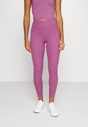 Ensemble de sport ajusté en violet clair uni. Tissu lisse et extensible. Haut court, leggings taille haute, associés à des baskets blanches.