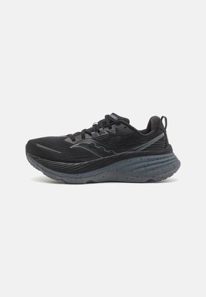 Zapatilla de running negra con un upper texturizado, suela gruesa con motas grises y detalles reflectantes en el lateral. Diseñada para la comodidad y el soporte.
