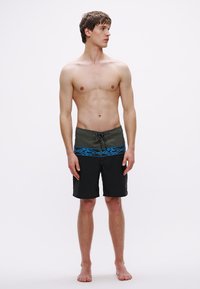 Μαγιό σορτς με σκούρο γκρι σχέδιο και μπλε εμπριμέ ζώνη μέσης, κατασκευασμένο από ελαφρύ, γρήγορα στεγνώνουσα υλικό.