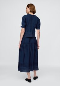 Vestido de dos piezas azul marino con mangas abullonadas, dobladillo de encaje bordado y falda con volante en capas. Vista trasera que muestra el corpiño ajustado y la tela fluida.