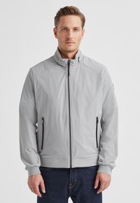 Hellgraue Reißverschlussjacke mit Stehkragen, elastischen Bündchen und zwei seitlichen Taschen mit schwarzen Reißverschlüssen. Glatte, matte Stoffstruktur.