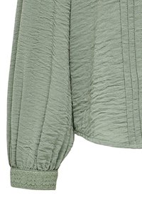 Light green blouse with textured fabric, featuring a folded design and embroidered cuff accents. Long, puffed sleeves complete the look.