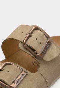 Sandale en daim beige avec deux brides réglables, munies de boucles en métal cuivré, et une semelle intérieure en liège profilée.