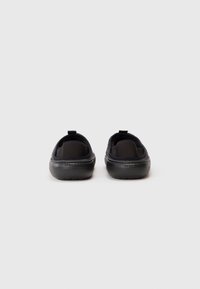 Fekete slip-on Crocs cipők hátulról bemutatva, texturált talppal és sarokhúzó fülekkel, fehér háttérrel.