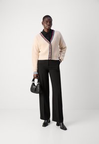 Maglione a coste crema con rifiniture colorate, camicia nera con colletto, pantaloni neri su misura e borsa nera. Stivaletti a punta completano l'outfit.