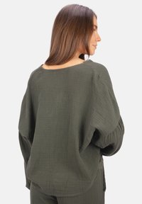 Luftiges, olivgrünes Oberteil aus strukturiertem Stoff; hat einen weiten Halsausschnitt, überschnittene Schultern und eine entspannte, fallende Silhouette.