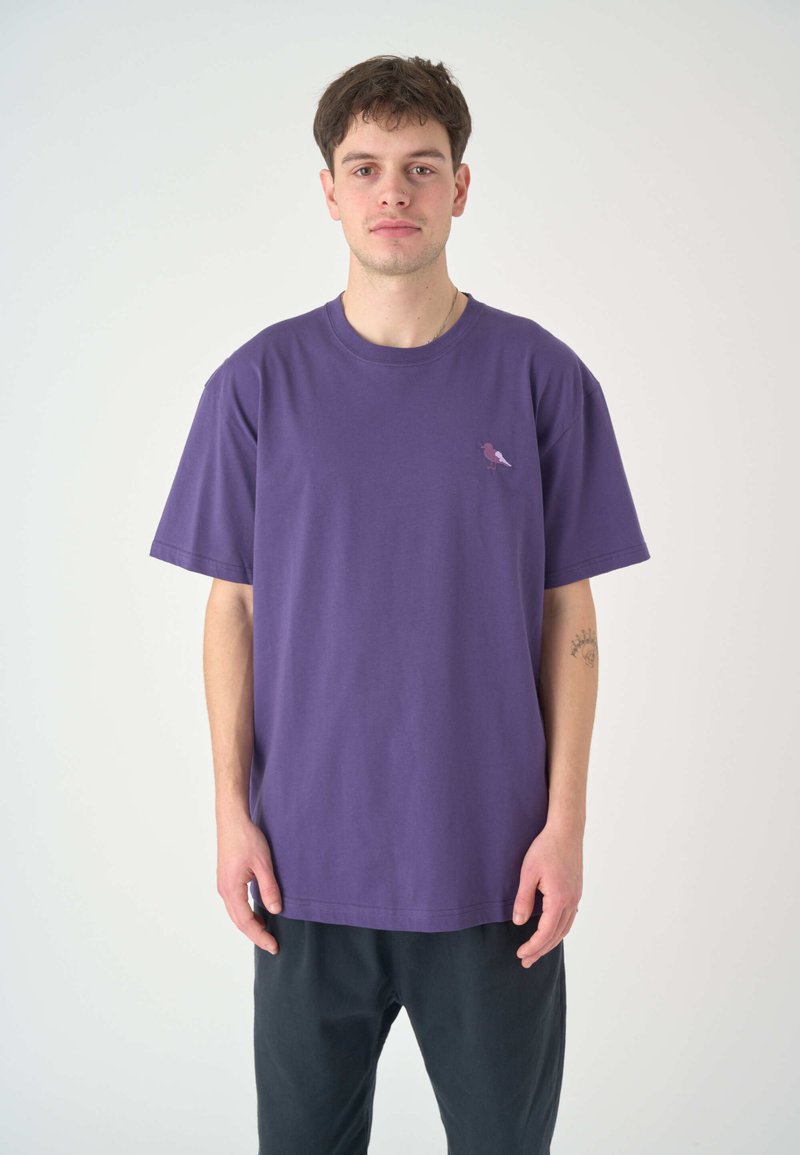Lila Baumwoll-T-Shirt mit kurzen Ärmeln und rundem Ausschnitt. Mit einem kleinen pinken und weißen Vogel-Graphic auf der Brust.