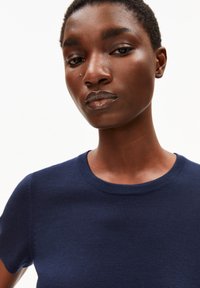 Donkerblauwe korte mouwen tricot top met een ronde hals en een gladde textuur. Close-up toont subtiele stikdetails op de schouders.