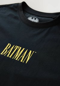 Čierne bavlnené tričko s veľkým žltým grafickým nápisom "BATMAN". Kruhový výstrih a krátke rukávy s hladkou textúrou.