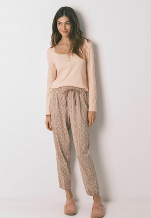 Hellrosa langärmliges Oberteil mit Knopfdetails, kombiniert mit gemusterten beigen Jogginghosen und pinken Hausschuhen, die eine lockere Passform und weichen Stoff zeigen.
