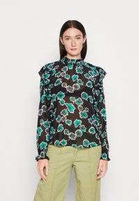 Schwarze Bluse mit floralem Muster aus transparentem Material, mit türkis- und rosa-blumen, mit Rüschenärmeln und einem figurbetonten Hals. Kombiniert mit hellgrünen Hosen.