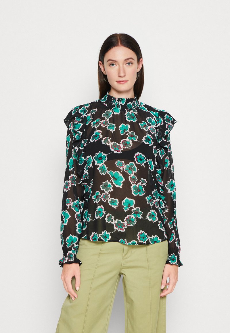Schwarze Bluse mit floralem Muster aus transparentem Material, mit türkis- und rosa-blumen, mit Rüschenärmeln und einem figurbetonten Hals. Kombiniert mit hellgrünen Hosen.