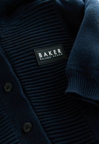 Gehaakte marineblauwe cardigan met ribbeltextuur, voorzien van een zwart label met "BAKER" in witte letters en zwarte knoopdetails.