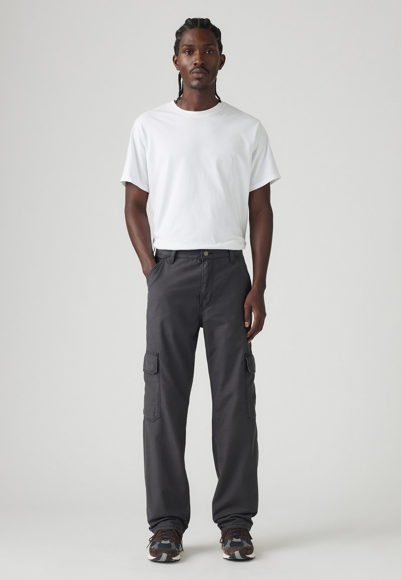 Camiseta blanca de manga corta combinada con pantalones cargo oscuros que cuentan con bolsillos laterales y un corte relajado, completada con zapatillas deportivas de patrón.