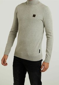 Pull à col roulé gris clair en maille lisse. Présente un petit patch logo marron sur la poitrine ainsi que des poignets et un ourlet côtelés.
