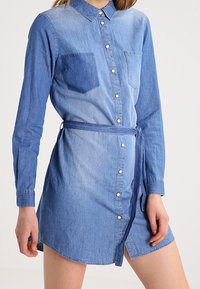 Denimskjortklänning med en gradient blå design, långa ärmar, knappstängning fram och ett knytbälte i midjan. Inkluderar en bröstficka.