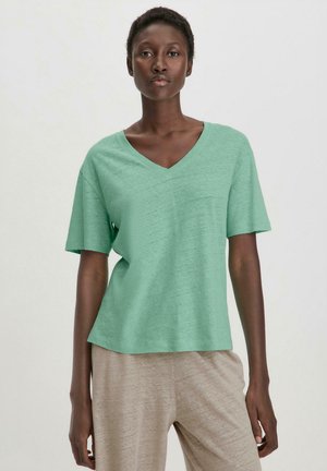 Minzgrünes T-Shirt mit kurzen Ärmeln und V-Ausschnitt, aus weichem Stoff, mit lässiger Passform und minimaler Textur, kombiniert mit beigen, lockeren Hosen.