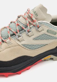 Trekking shoe with a beige suede and mesh upper, grey accents, red laces, and a black rubber sole featuring multi-directional lugs for traction.