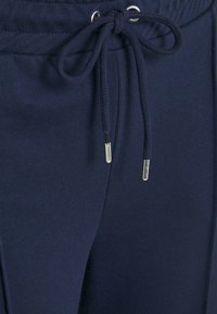 Pantaloni della tuta blu navy con vita elasticizzata, cordoncino regolabile e estremità metalliche. Tessuto morbido e liscio con tasche laterali.