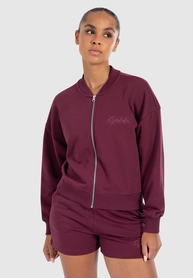 Sweatshirt bordeaux zippé avec bords côtelés et détail de logo, associé à un short coordonné. Design doux et décontracté, idéal pour une tenue de loisirs.