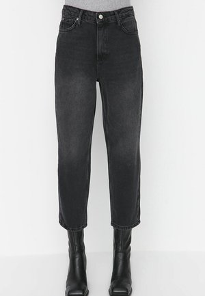 Sorte højttaljede jeans med lige ben, båret med sorte støvler med firkantet tå, vist fra talje til fødder mod en hvid baggrund.