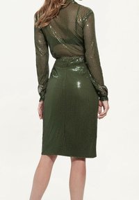 Zielona sukienka pokryta cekinami o dopasowanej sylwetce, z długimi rękawami i krojem ołówkowym. Tkanina ma błyszczący, teksturowany wygląd.